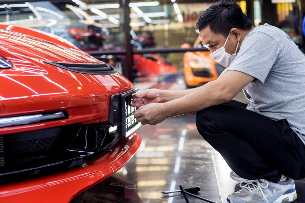 A mechanic reinstalls a car’s front license plate.
